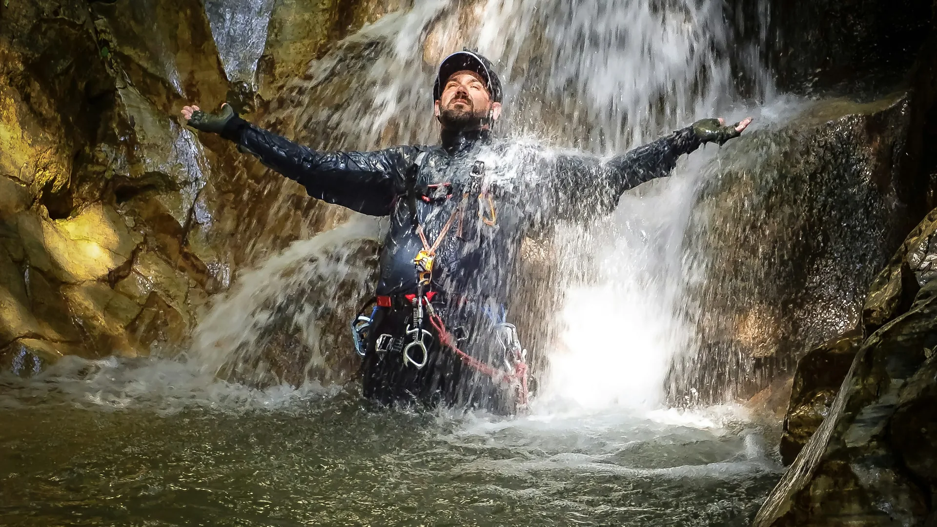 A canyoner in a wetsuit sliding down a waterfall into a turquoise gorge pool near Interlaken