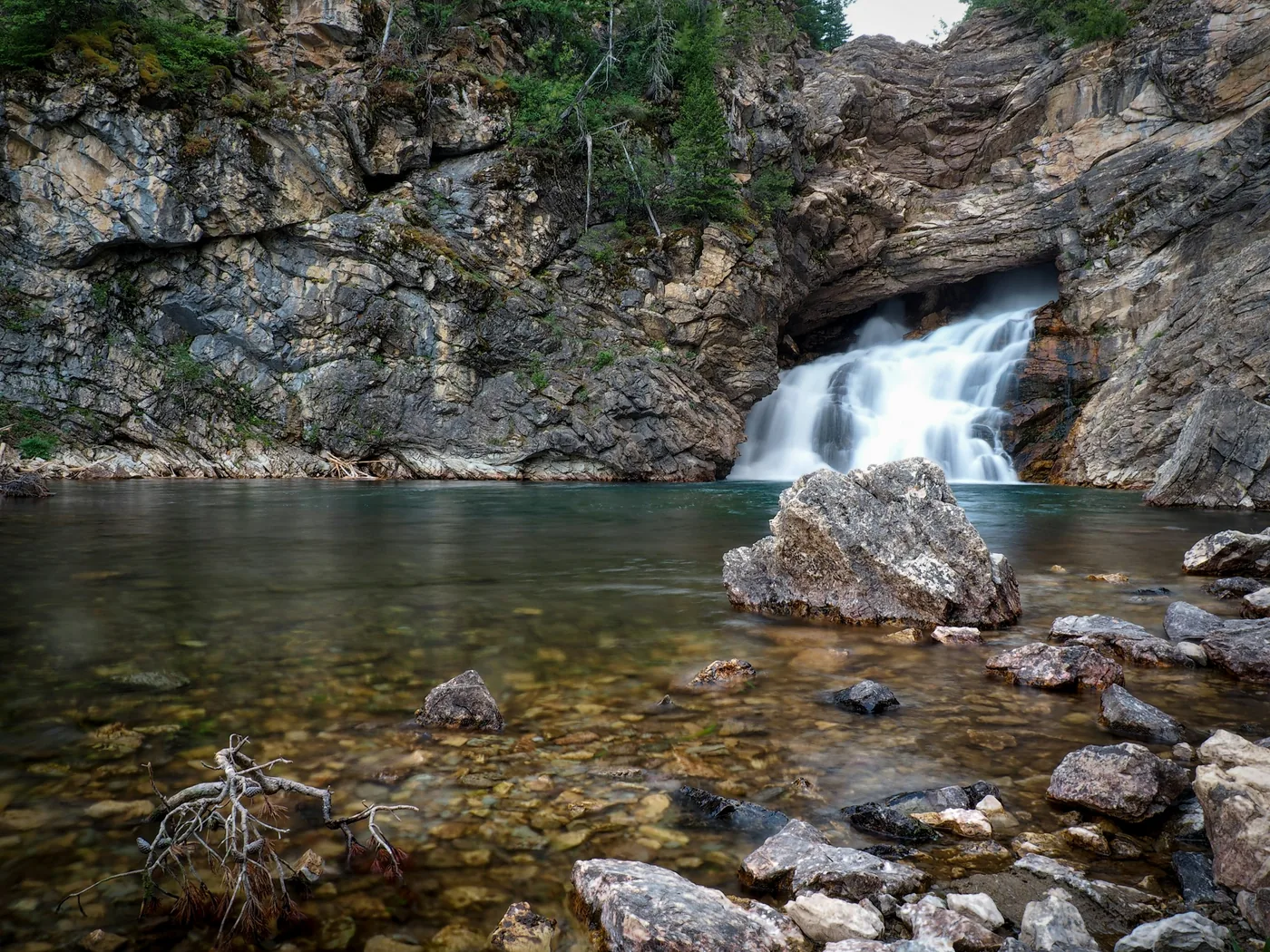 A waterfall dropping into a deep pool in an alpine canyon